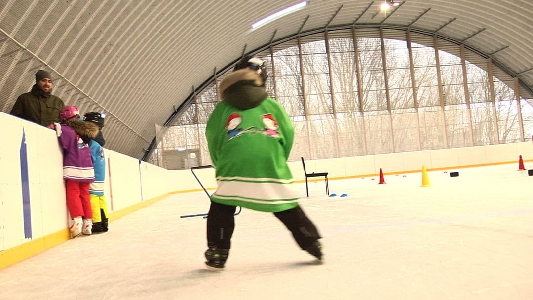 Děti trénující bruslení v obloukové montované ocelové sportovní hale ve městě Hurbanovo na Slovensku. Moderní krytá ledová plocha určená pro výuku bruslení a hokejový trénink.