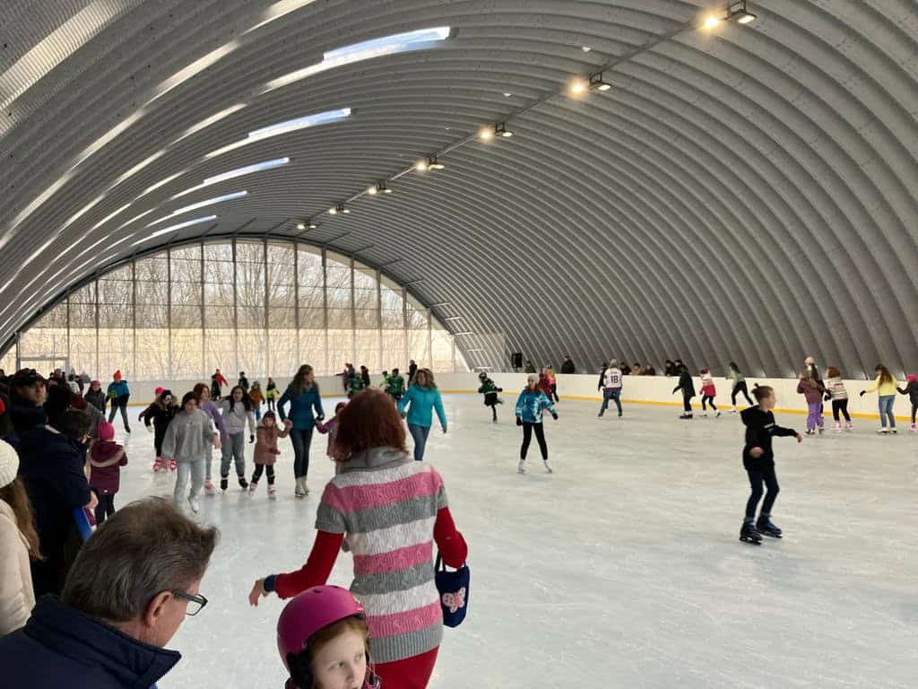 Veřejné bruslení v moderní obloukové montované ocelové sportovní hale ve městě Hurbanovo na Slovensku. Lidé všech věkových kategorií si užívají bruslení na kryté ledové ploše.