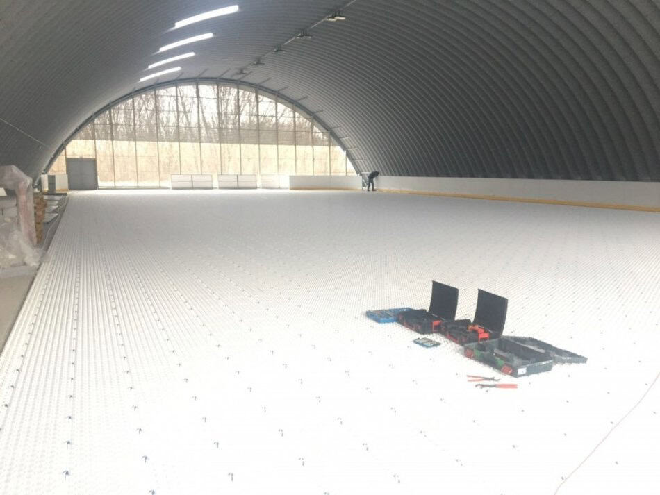 Montáž ledové plochy v obloukové montované ocelové sportovní hale ve městě Hurbanovo na Slovensku. Práce na instalaci chladicího systému a příprava na provoz zimního stadionu.