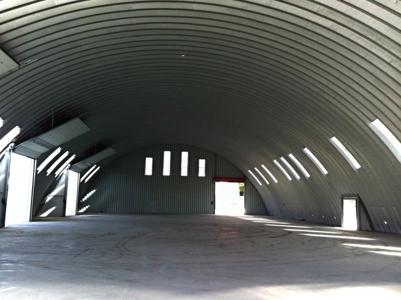 Interiér ocelové obloukové skladové haly s otevřenými vraty a přirozeným denním světlem, realizace HUPRO SYSTEMS SE