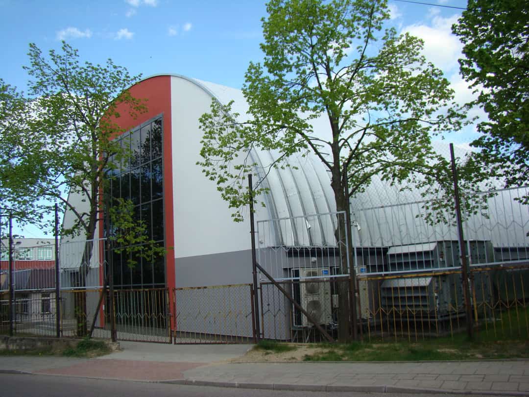 Montovaná ocelová víceúčelová sportovní hala Bielostok, boční pohled na obloukovou konstrukci s proskleným vstupem a moderním designem. Realizace společnosti HUPRO SYSTEMS SE.