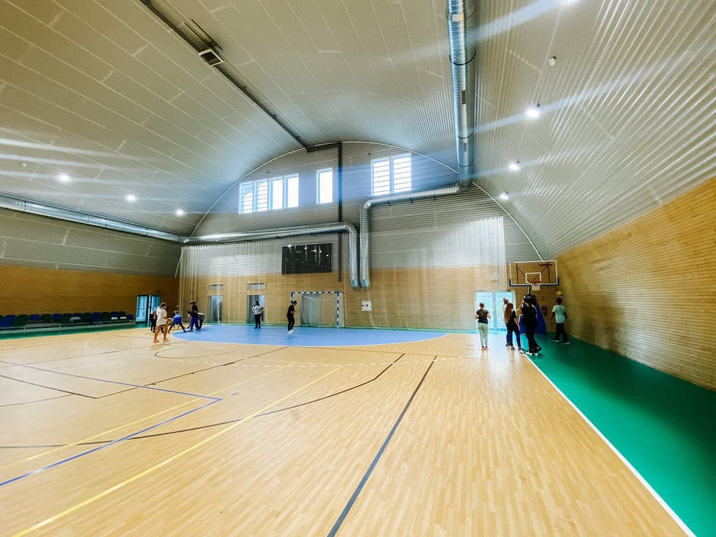 Interiér moderní sportovní haly ve městě Bytča na Slovensku s dřevěným obložením, víceúčelovým hřištěm a tribunou, realizace od HUPRO SYSTEMS SE.