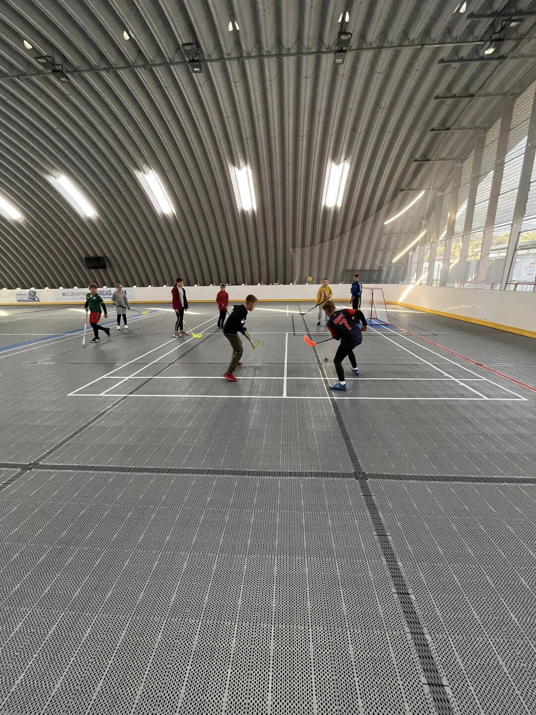 Děti hrají florbal v multifunkční montované hale v Hriňové s plastovým sportovním povrchem od společnosti HUPRO SYSTEMS SE, vhodné pro školní i klubové využití.