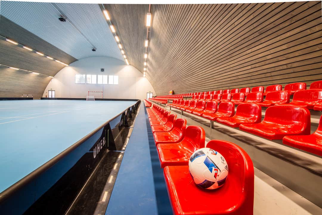 Tribuny s červenými sedadly a míčem v obloukové montované ocelové sportovní hale v Kežmarku postavené systémem HUPRO SYSTEMS SE