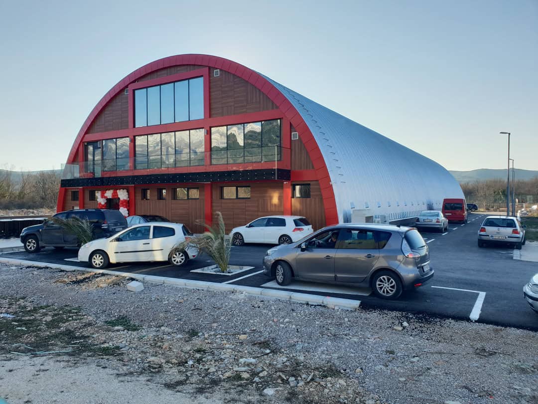 Montovaná ocelová oblouková sportovní hala Kotor – moderní hala s červenými detaily a proskleným čelním průčelím, realizace HUPRO SYSTEMS SE.