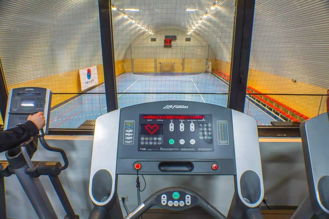 Montovaná ocelová oblouková sportovní hala Kotor – pohled z fitness zóny na hlavní hrací plochu přes prosklenou stěnu, realizace HUPRO SYSTEMS SE.