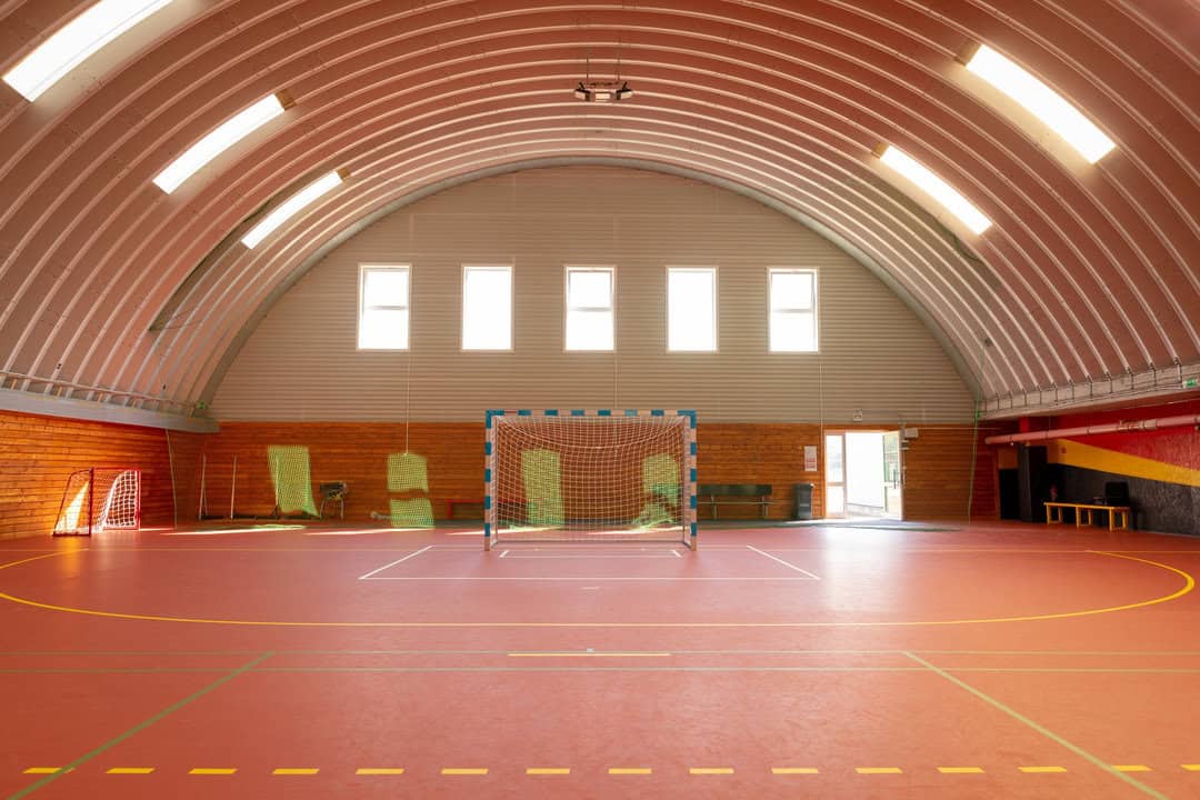 Interiér obloukové montované ocelové sportovní haly v Bratislavě Ružinově s červeným povrchem hřiště a brankou pro míčové sporty, postavené systémem HUPRO SYSTEMS SE.