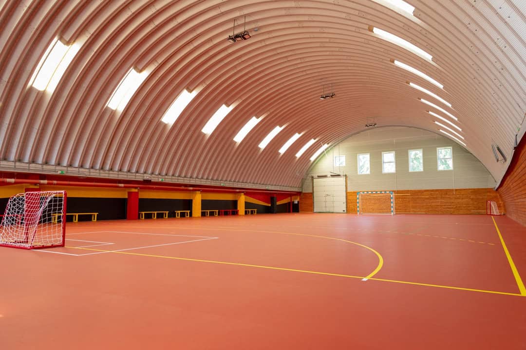Interiér obloukové montované ocelové sportovní haly v Bratislavě Ružinově s červeným povrchem hřiště, brankami a dřevěným obložením stěn, postavené systémem HUPRO SYSTEMS SE.