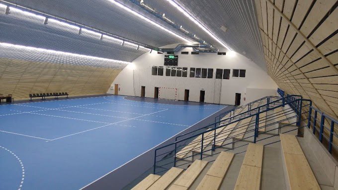 Pohled z tribuny na víceúčelovou sportovní halu Brno Maloměřice s modrým povrchem a dřevěným obložením stěn, realizace HUPRO SYSTEMS SE.