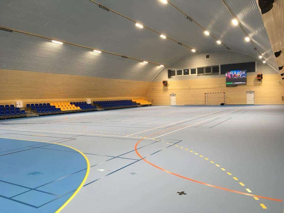 Interiér ocelové obloukové sportovní haly v Kynžvartu s multifunkčním hřištěm, tribunou a dřevěným obložením stěn, realizace HUPRO SYSTEMS SE.