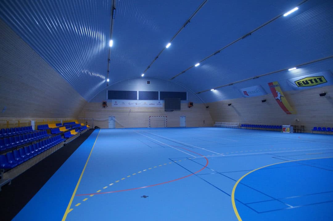 Ocelová montovaná sportovní hala v Kynžvartu s modrým povrchem hřiště, tribunou a dřevěným obložením stěn, realizace HUPRO SYSTEMS SE.