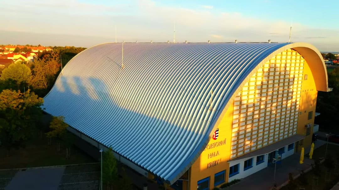 Oblouková sportovní hala Praha Kbely s moderní ocelovou konstrukcí a žlutou fasádou, realizace HUPRO SYSTEMS SE