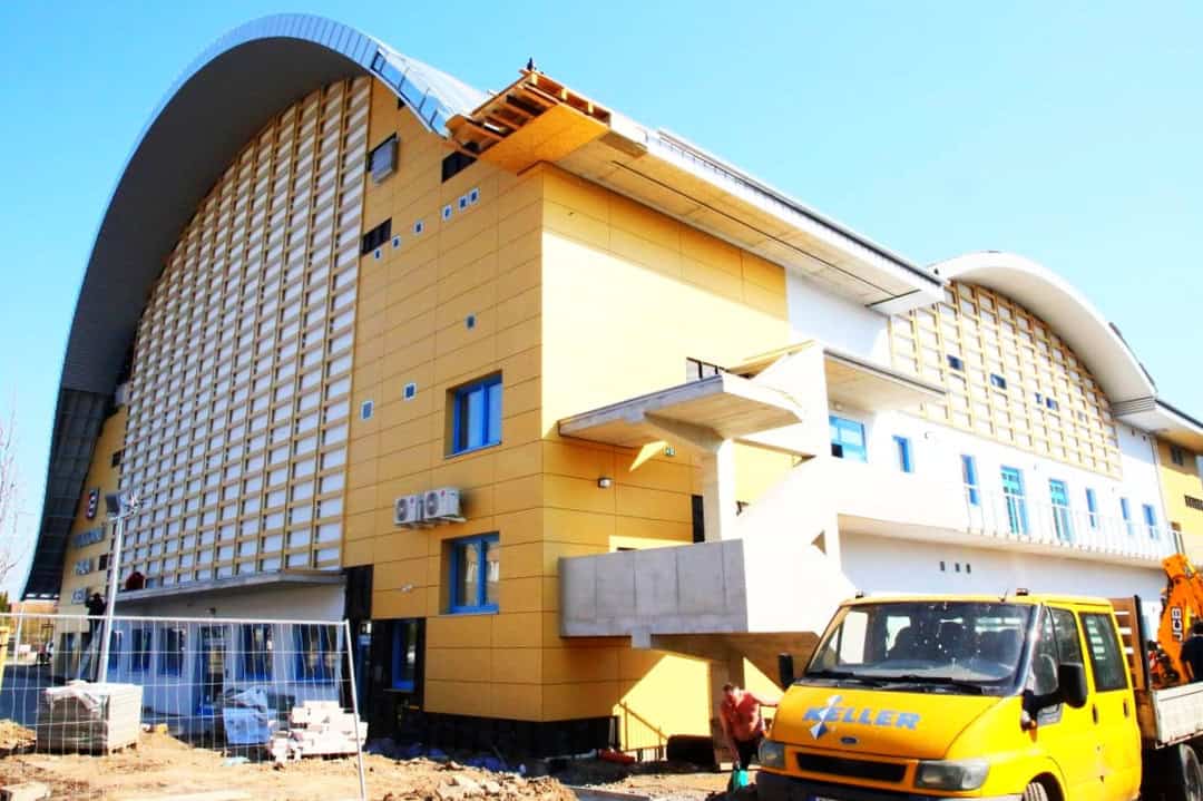 Sportovní hala Praha Kbely během výstavby, pohled na žlutou fasádu a charakteristickou obloukovou střechu, realizace HUPRO SYSTEMS SE