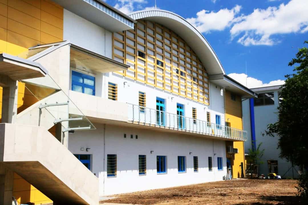 Moderní oblouková montovaná ocelová sportovní hala Praha Kbely s proskleným schodištěm a architektonickými detaily v bílo-žlutém provedení.