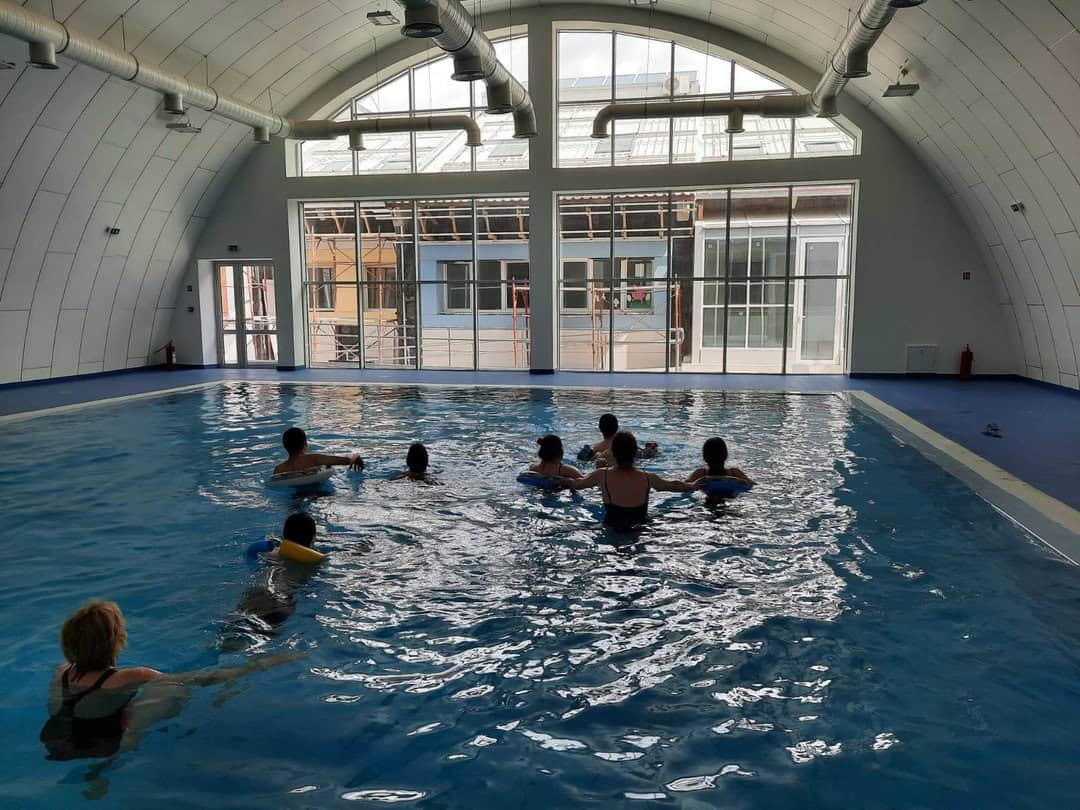 Montovaná ocelová plavecká hala Subotica – interiér bazénu s prosklenou čelní stěnou při výuce plavání, realizace HUPRO SYSTEMS SE.