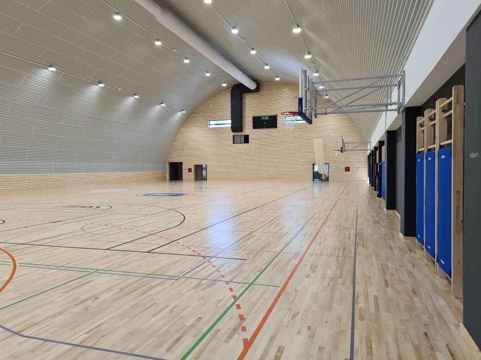 Víceúčelová montovaná ocelová sportovní hala Koprivnica, moderní interiér s basketbalovým hřištěm, dřevěnou podlahou a ocelovou konstrukcí HUPRO SYSTEMS SE.