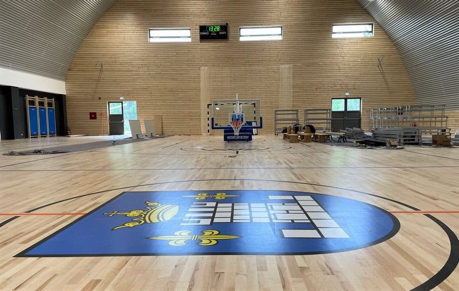 Víceúčelová montovaná ocelová sportovní hala Koprivnica, interiér s basketbalovým hřištěm a logem města, moderní sportovní hala HUPRO SYSTEMS SE.