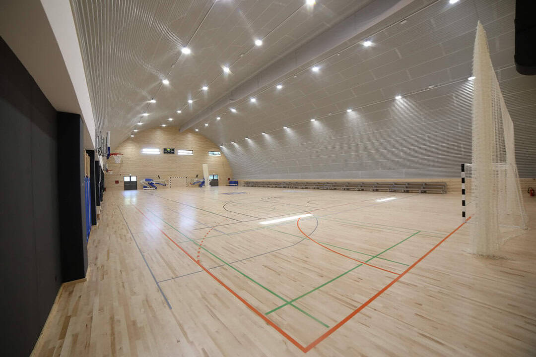 Víceúčelová montovaná ocelová sportovní hala Koprivnica, interiér s dřevěnou sportovní podlahou, basketbalovými koši a tribunou pro diváky, realizace HUPRO SYSTEMS SE.
