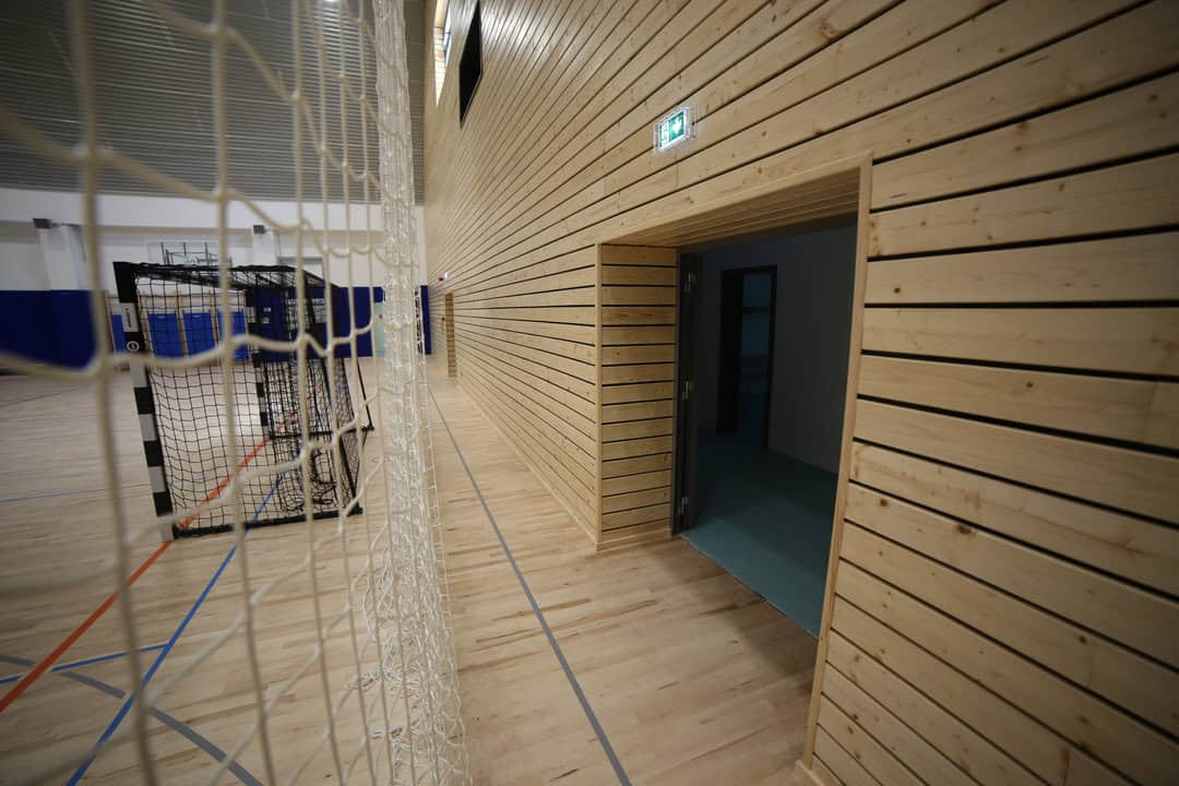 Oblouková sportovní hala Křiževci, interiér s dřevěným obložením stěn, brankami a sportovní palubovkou, realizace HUPRO SYSTEMS SE.