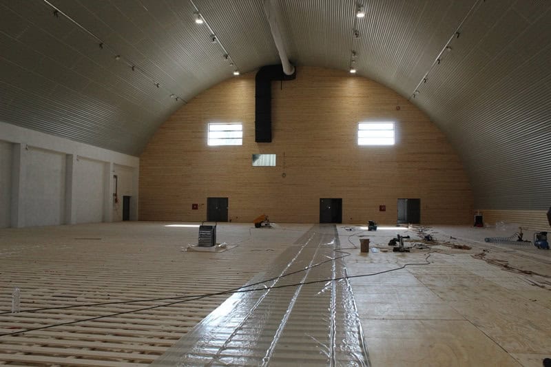 Oblouková sportovní hala Křiževci ve fázi výstavby, interiér s dřevěným obložením stěn a rozestavěnou sportovní podlahou, realizace HUPRO SYSTEMS SE.