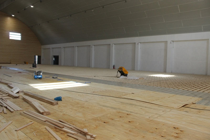 Oblouková sportovní hala Křiževci v průběhu výstavby, interiér s rozpracovanou dřevěnou podlahou a montážní technikou, realizace HUPRO SYSTEMS SE.