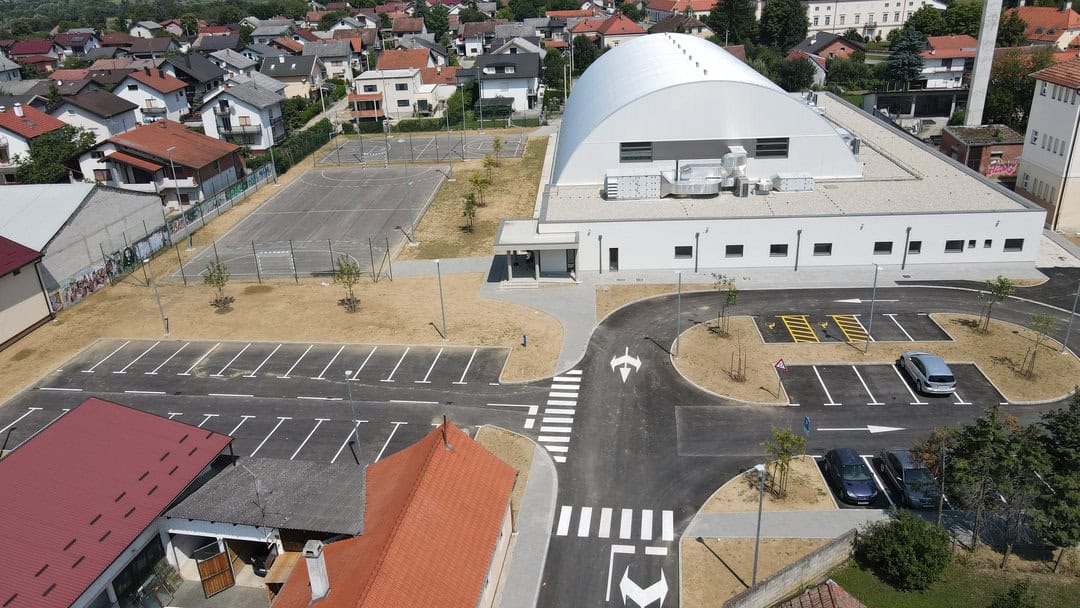 Víceúčelová montovaná ocelová sportovní hala Križevci, letecký pohled na moderní sportovní objekt s parkovištěm a venkovním hřištěm, realizace HUPRO SYSTEMS SE.
