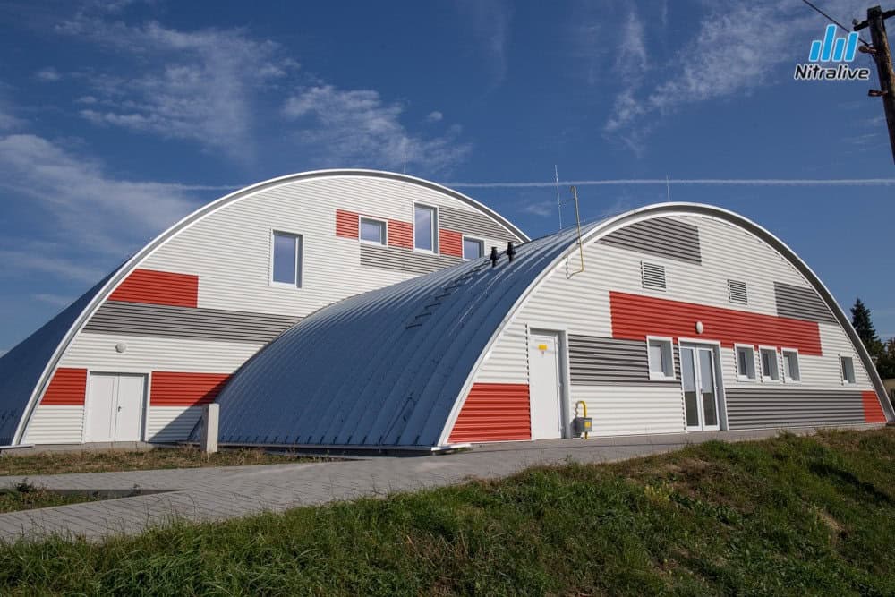 Sportovní hala Nitra Tulipanová – moderní montovaná oblouková stavba HUPRO SYSTEMS SE s výrazným červeno-šedým obkladem fasády a energeticky úsporným řešením.