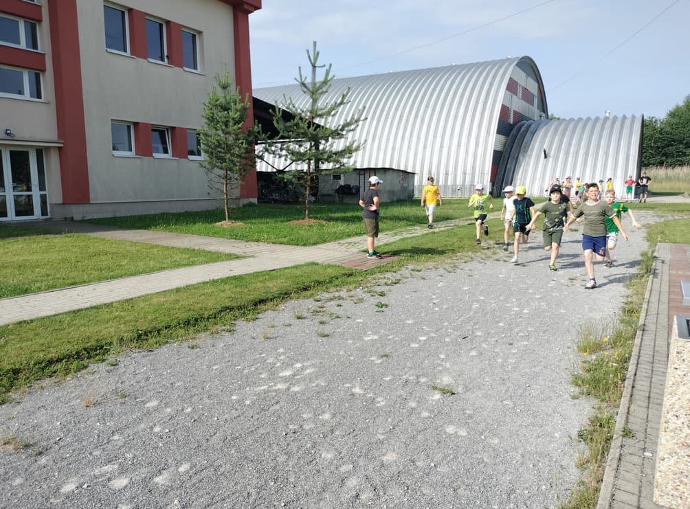 Sportovní hala v Radoľe s obloukovou montovanou konstrukcí od HUPRO SYSTEMS SE, děti běží po areálu u haly během sportovních aktivit.