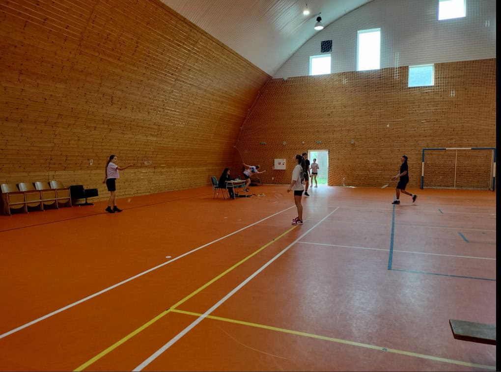 Sportovní hala v Radoľe s dřevěným obložením stěn a oranžovým povrchem, hráči hrají badminton na multifunkčním hřišti v montované konstrukci od HUPRO SYSTEMS SE.