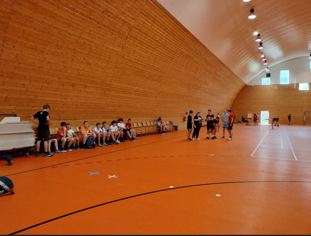 Interiér sportovní haly Radoľa s dřevěným obložením a oranžovým povrchem, trénink mladých sportovců v multifunkční hale s montovanou konstrukcí HUPRO SYSTEMS SE.