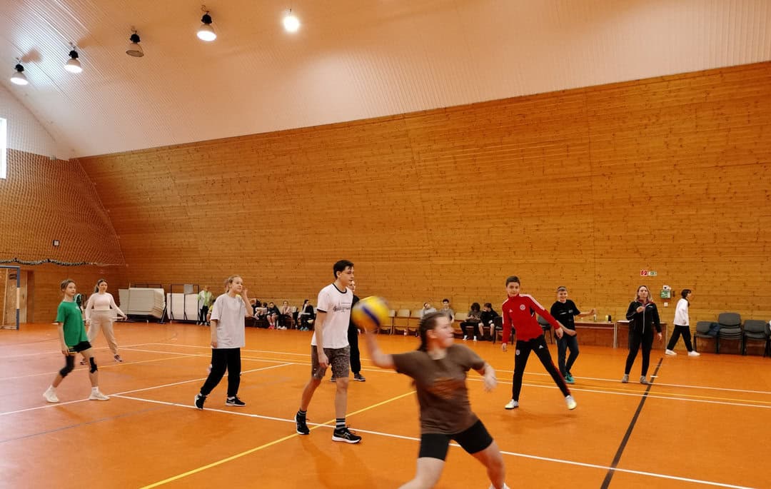Sportovní hala v Radoľe s dřevěným obložením a oranžovým sportovním povrchem, žáci hrají vybíjenou v moderní multifunkční hale realizované společností HUPRO SYSTEMS SE.