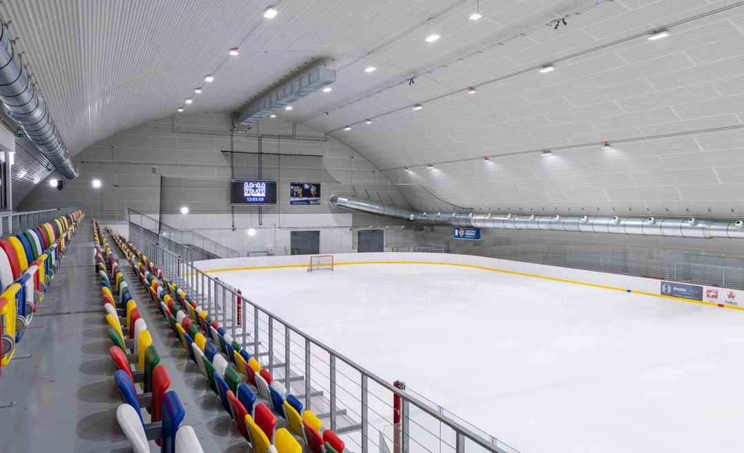 Interiér Zimního stadionu Vyškov – moderní ledová plocha s tribunami a barevnými sedačkami v obloukové montované ocelové hale realizované firmou HUPRO SYSTEMS SE.