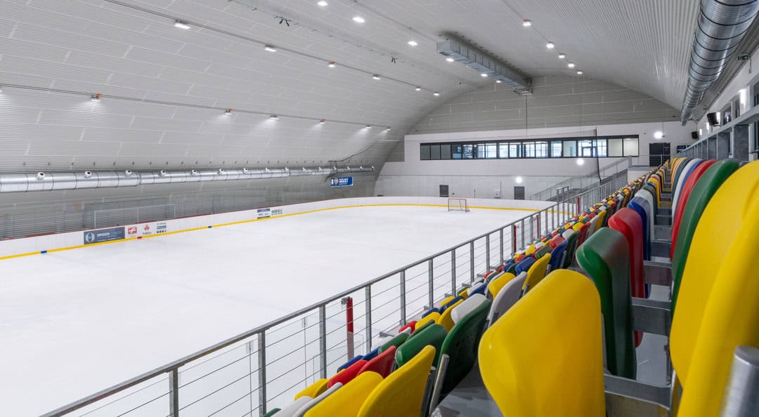 Interiér Zimního stadionu Vyškov – moderní ledová plocha s barevnými sedačkami a prosklenou tribunou v obloukové montované ocelové hale od firmy HUPRO SYSTEMS SE.