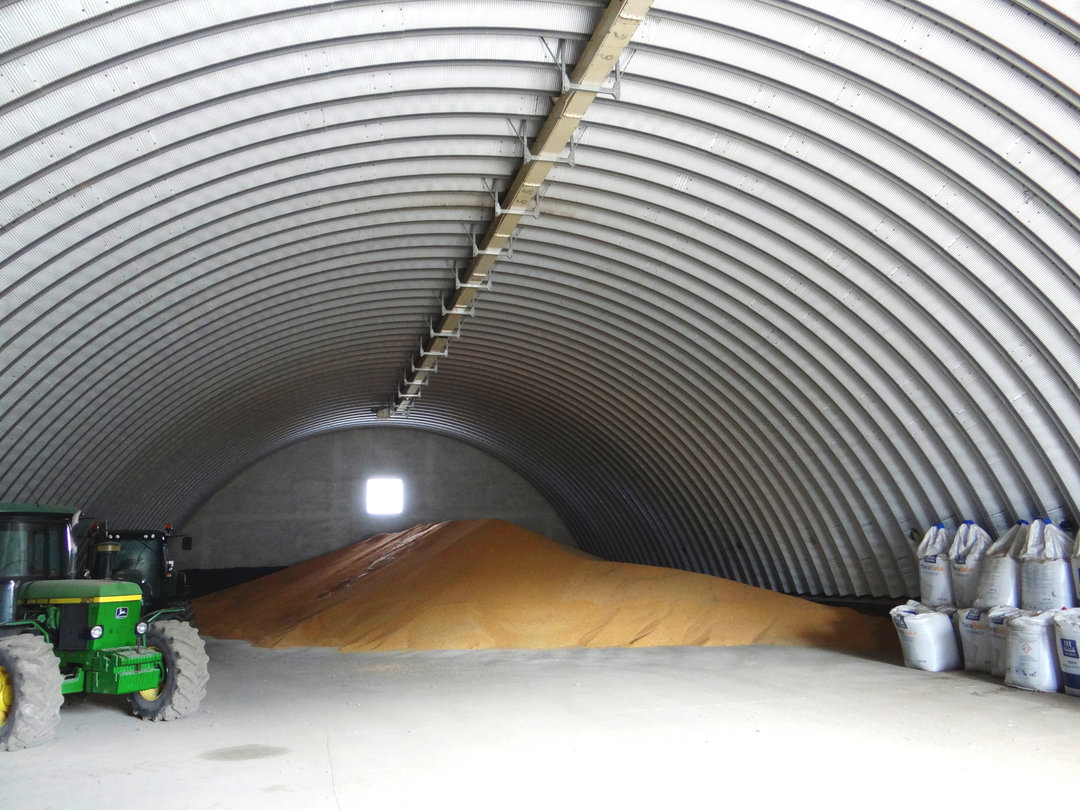 Wnętrze montowanej stalowej łukowej hali rolniczej ze składowanym zbożem, ciągnikiem i workami typu big bag. Realizacja firmy HUPRO SYSTEMS SE. Wnętrze montowanej stalowej łukowej hali rolniczej ze składowanym zbożem, ciągnikiem i workami typu big bag. Realizacja firmy HUPRO SYSTEMS SE.