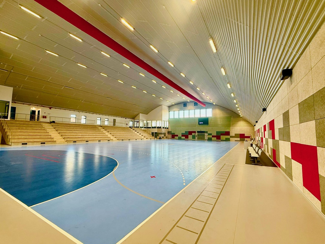 Wnętrze hali sportowej Nové Bránice z niebieskim boiskiem, drewnianymi trybunami i panelami akustycznymi. Realizacja firmy HUPRO SYSTEMS SE. Wnętrze hali sportowej Nové Bránice z niebieskim boiskiem, drewnianymi trybunami i panelami akustycznymi. Realizacja firmy HUPRO SYSTEMS SE.