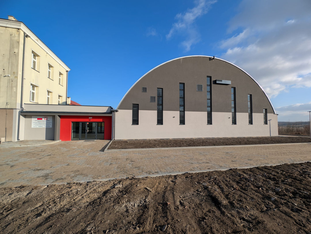Montowana stalowa łukowa hala sportowa Szaniec połączona z budynkiem szkoły, widok na wejście. Realizacja firmy HUPRO SYSTEMS SE. Montowana stalowa łukowa hala sportowa Szaniec połączona z budynkiem szkoły, widok na wejście. Realizacja firmy HUPRO SYSTEMS SE.