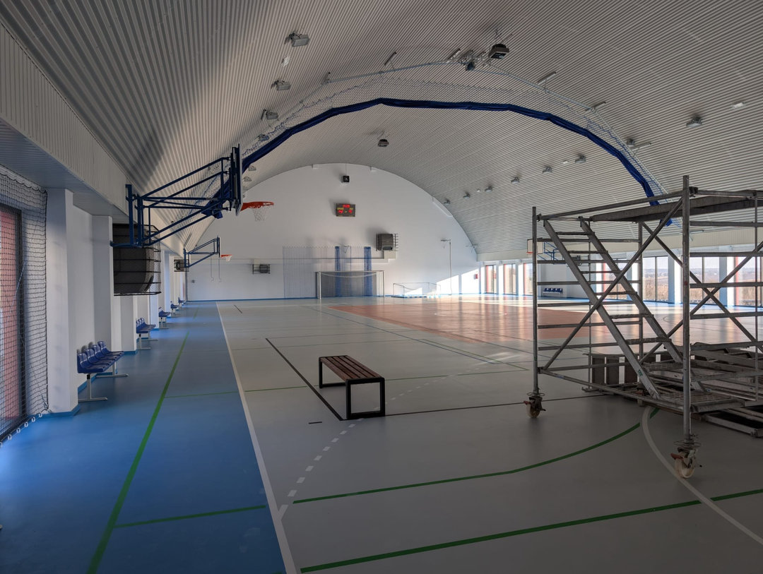 Przestronne wnętrze montowanej hali sportowej Szaniec z wyposażeniem do koszykówki, siatkami ochronnymi i łukową konstrukcją stalową. Realizacja firmy HUPRO SYSTEMS SE. Przestronne wnętrze montowanej hali sportowej Szaniec z wyposażeniem do koszykówki, siatkami ochronnymi i łukową konstrukcją stalową. Realizacja firmy HUPRO SYSTEMS SE.